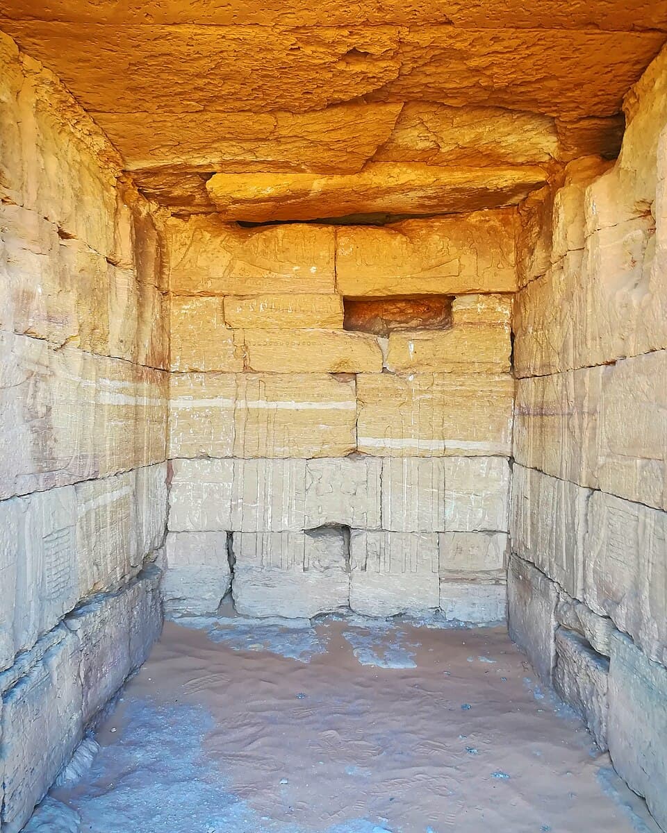 Inside the offering chapel of a Meroitic pyramid, sunlight catches the carved sandstone walls where reliefs — now weathered by two thousand years of desert wind — once depicted the deceased ruler receiving offerings for the afterlife. Few visitors ever step into these intimate inner chambers, making this a rare glimpse behind the pyramid's imposing façade.
