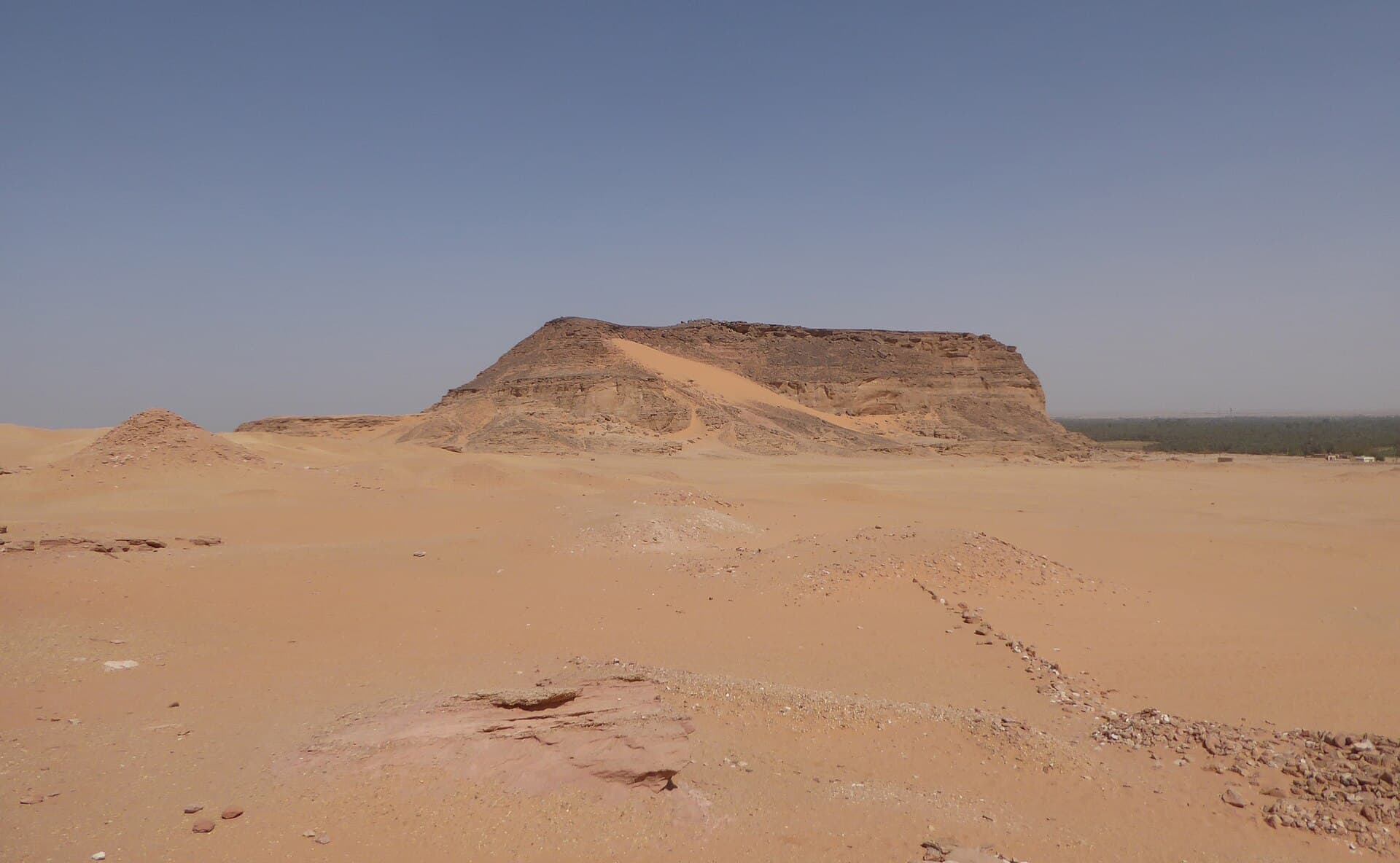 Seen from a distance across the desert plain, Jebel Barkal's flat-topped silhouette dominates the horizon, with the small pyramids of the surrounding Napatan-era cemeteries scattered before it.