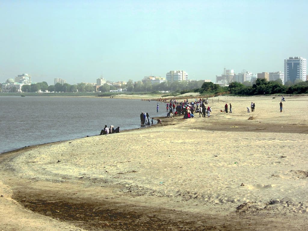 On weekends, families gather along Tuti Island's Blue Nile beach — a quiet stretch of sand where children play in the shallows and the Khartoum skyline rises just across the water.